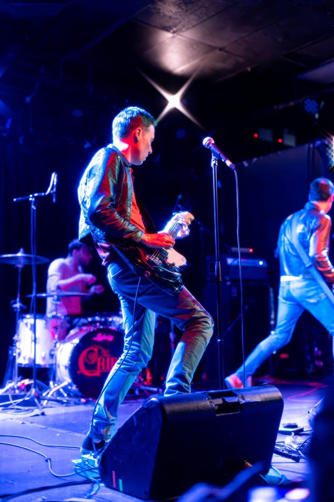 The Cribs' Ryan Jarman leans back with one foot on a monitor wedge, playing guitar beside the band's Ludwig kit in red and blue light at Lee's Palace, Toronto