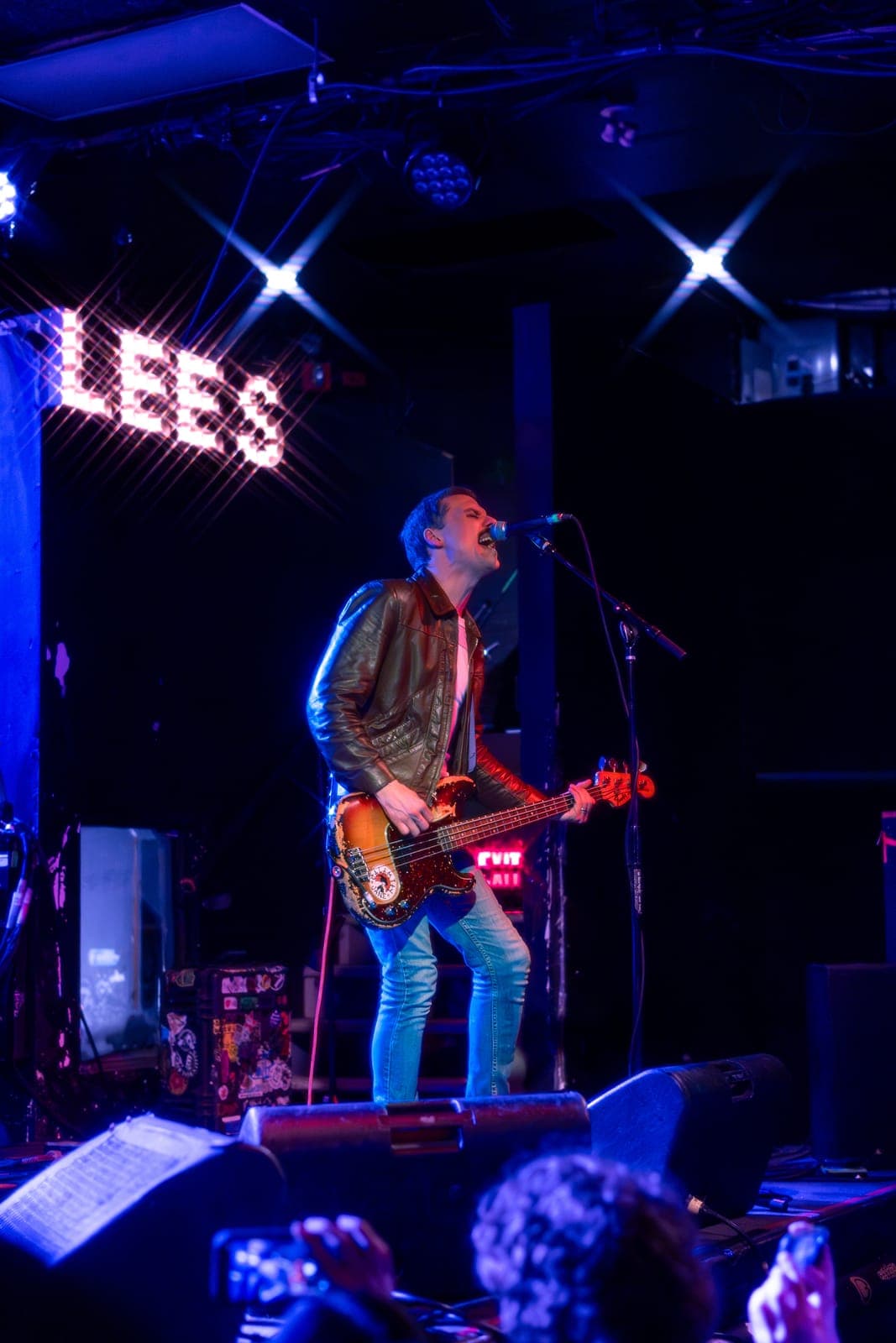 The Cribs' Gary Jarman sings into the mic with a sunburst Fender Precision bass beneath the 'LEES' marquee as fans film from the front row at Lee's Palace in Toronto
