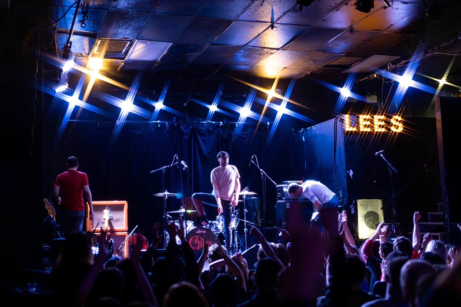 The Cribs' Ross Jarman stands atop the kick-drum riser, about to fling a drumstick into a sea of raised hands, as the band plays on under the 'LEES' marquee at Lee's Palace in Toronto