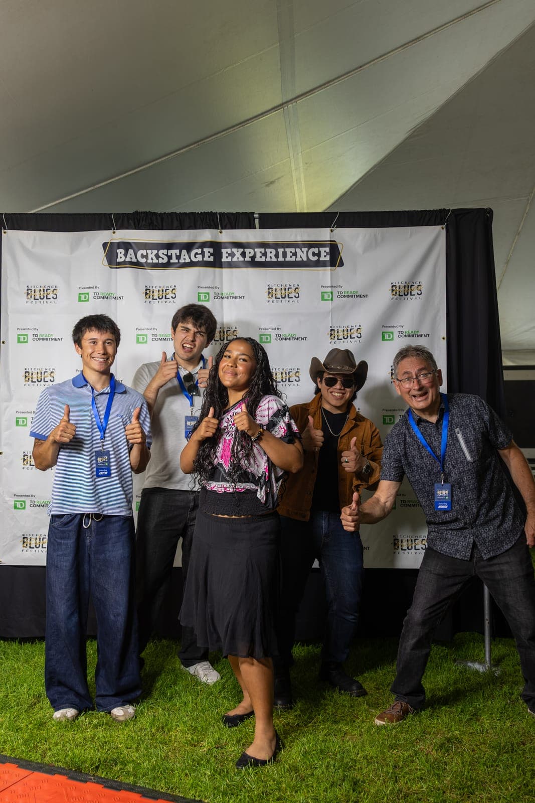 Isy Aboagye and her four bandmates give thumbs-up for a group photo in front of the 'Backstage Experience' banner at Kitchener Blues Festival
