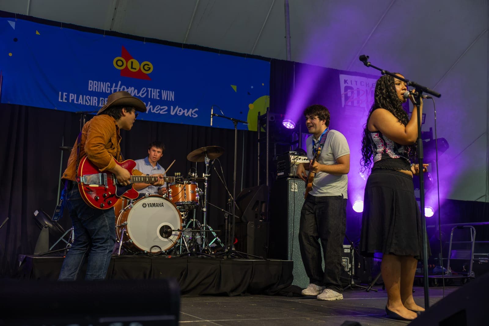 Isy Aboagye's guitarist and bassist stride cheerfully toward each other across the stage under purple light at Kitchener Blues Festival