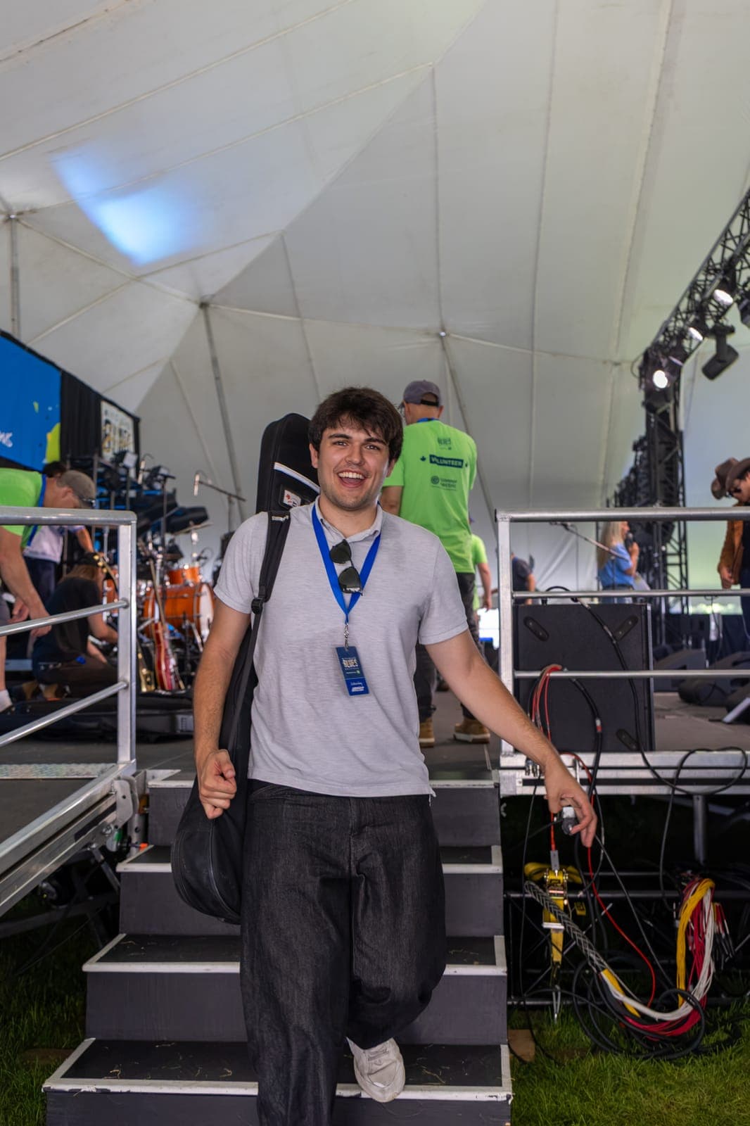 A member of Isy Aboagye's band grins as he carries a guitar case down the backstage stairs at Kitchener Blues Festival