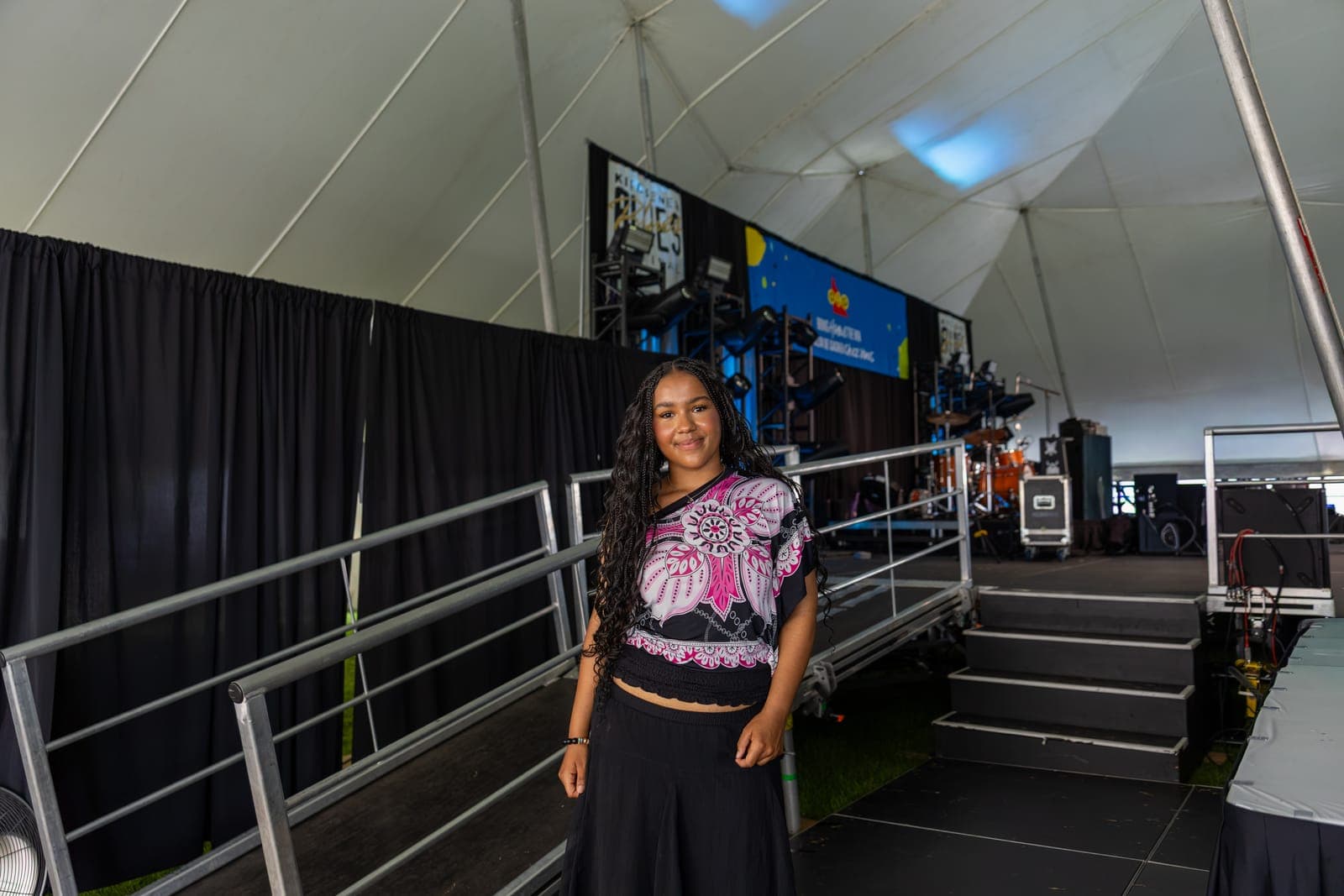 Isy Aboagye poses beside the stage ramp backstage at Kitchener Blues Festival, the drum kit and video screens visible behind her