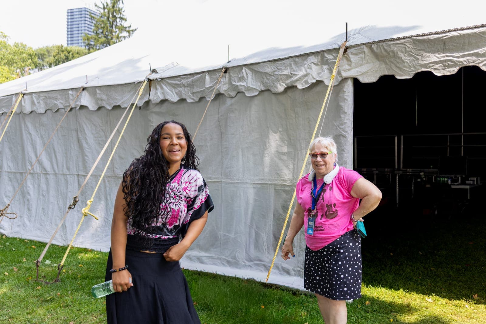 Isy Aboagye laughs beside a smiling festival volunteer outside the big-top tent at Kitchener Blues Festival, downtown Kitchener rising in the background