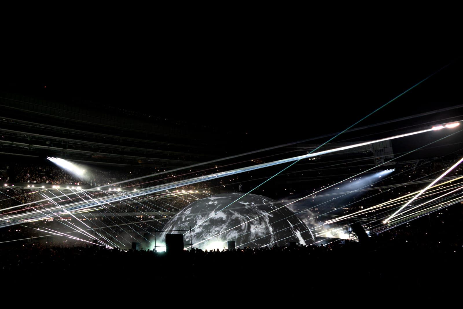 White laser beams rake across Soldier Field in every direction, converging on the glowing globe at the centre of the stadium floor