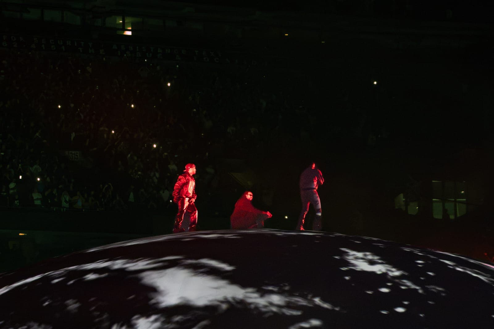 Big Sean, 2Chainz and Ye in red move across the dome as the lit crowd tiers of Soldier Field glow behind them