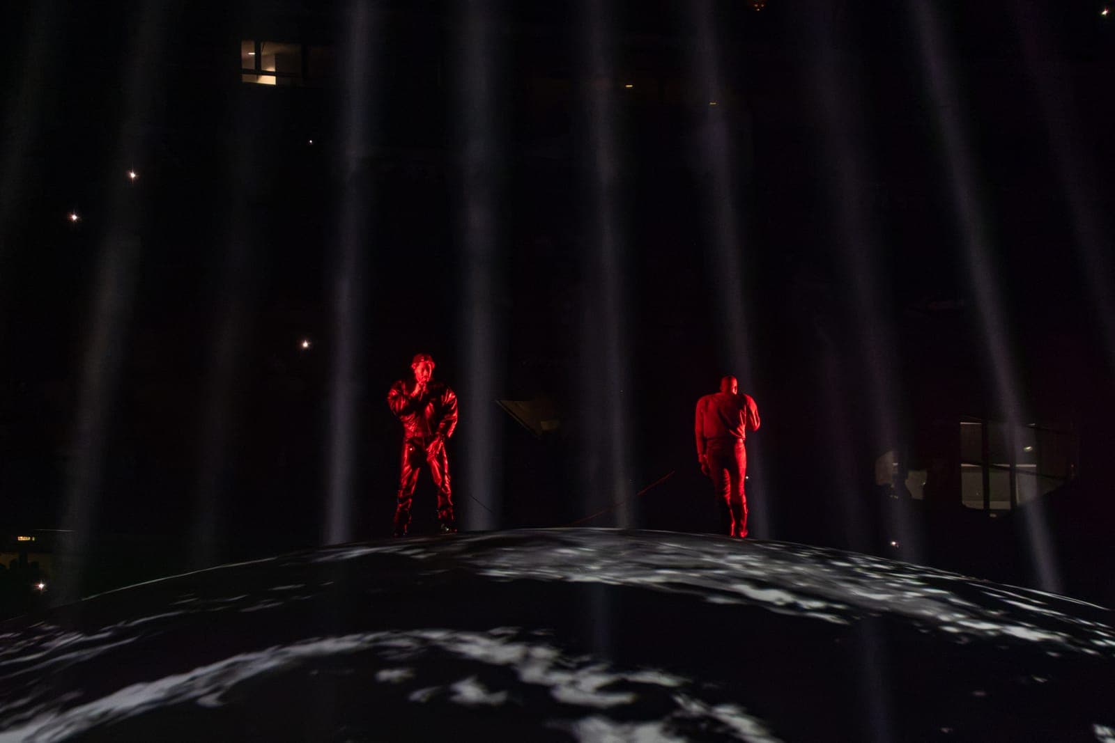 Common and Ye in red face each other across the top of the globe, vertical beams of light falling between them