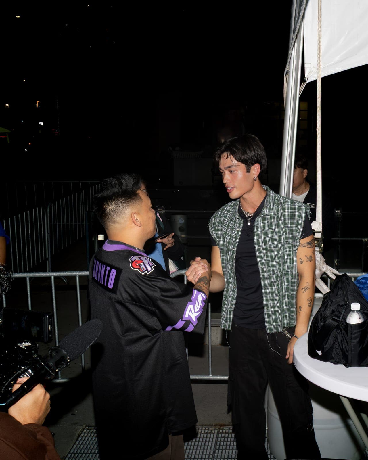 AJ Rafael clasps hands with another artist backstage by the tents at Philippine Festival Mississauga, a camera operator filming at the left