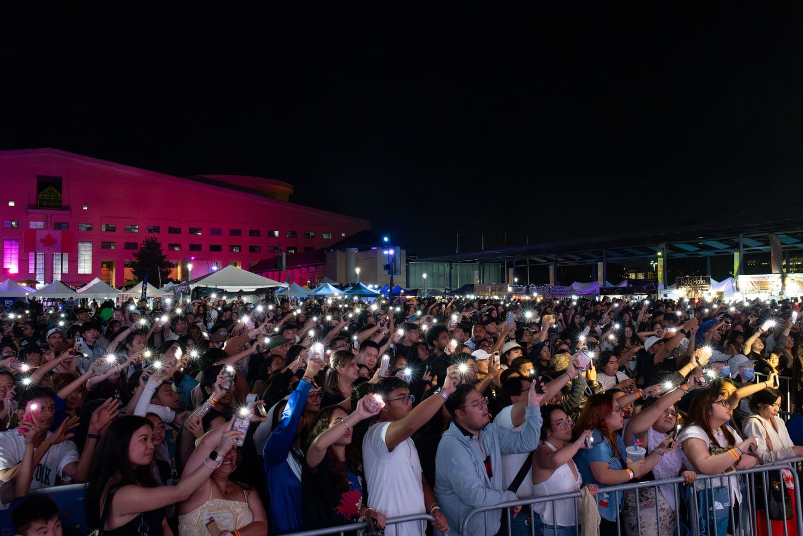 The Philippine Festival Mississauga crowd lifts phone flashlights across Celebration Square, the Civic Centre washed pink and food stalls glowing along the far side