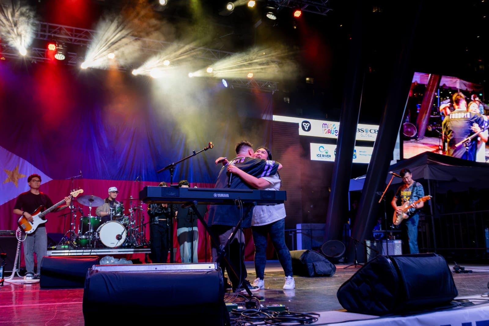 AJ Rafael pulls a fan into a hug behind his Yamaha keyboard on stage, the moment mirrored on the big screen beside them