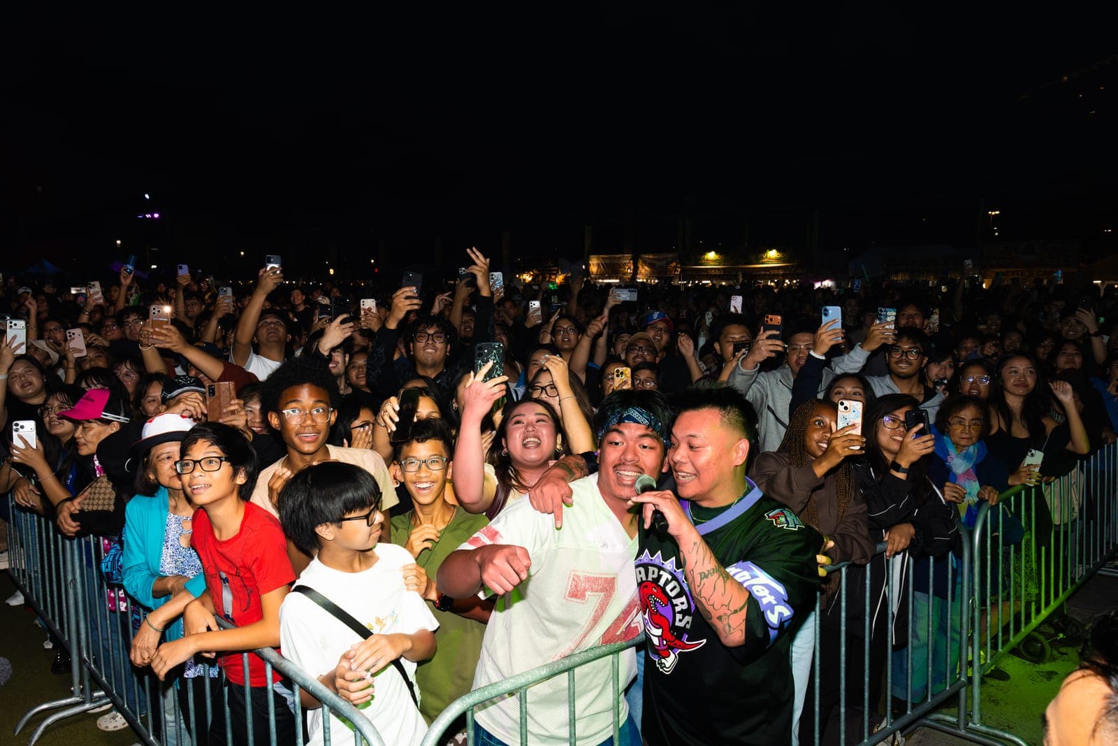 AJ Rafael sings into his mic on stage right beside a grinning fan in a bandana, families packed along the barricade at Philippine Festival Mississauga