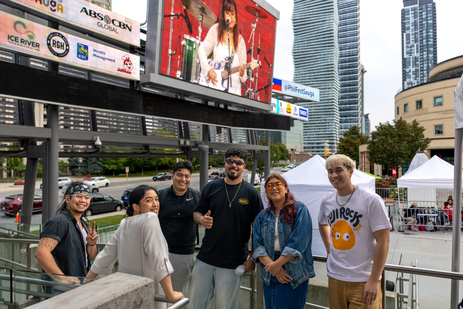 Simplé pose together on the walkway above Celebration Square, the festival screen behind them showing their own set and the @PhilFestSauga handle