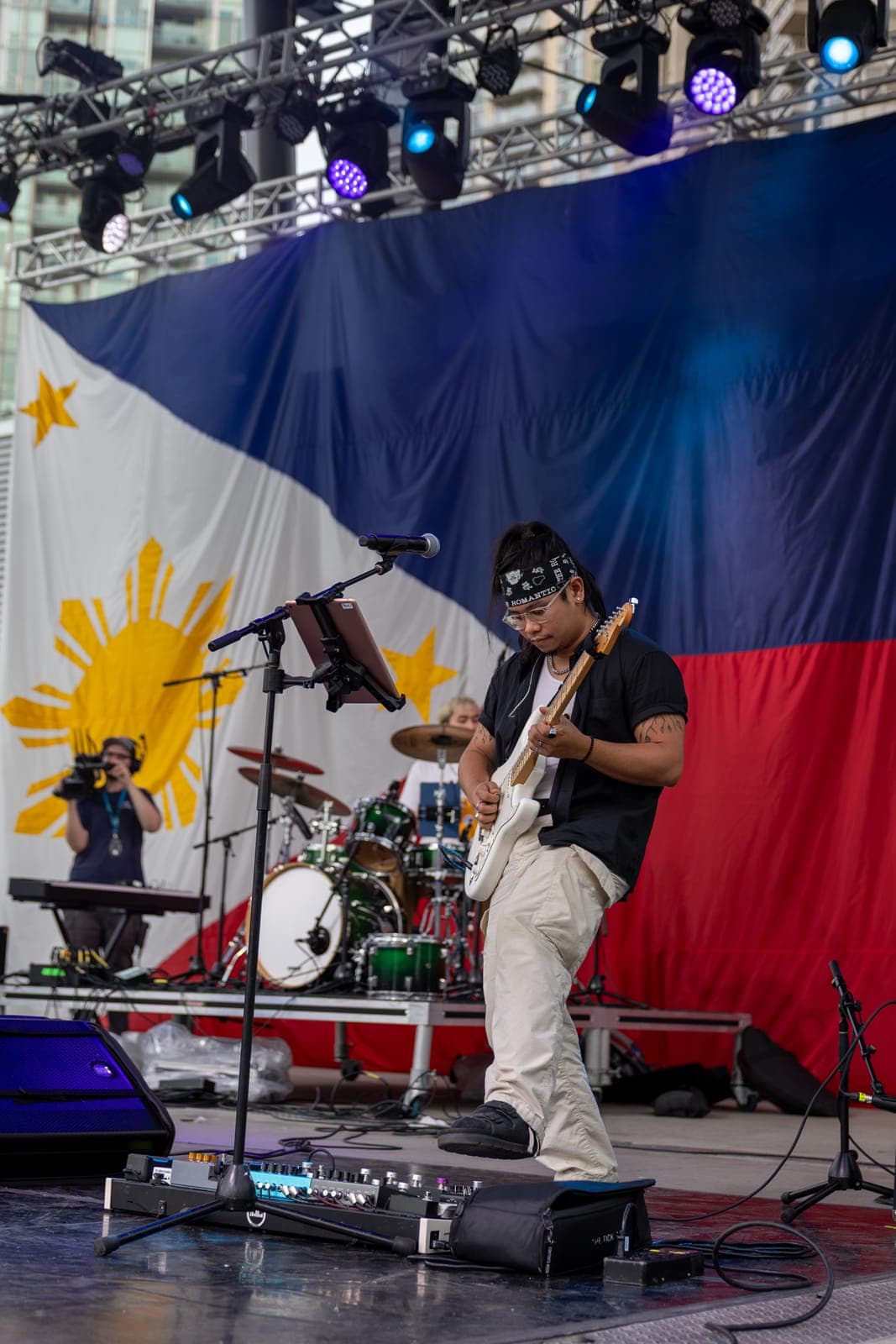 Simplé's guitarist digs into a white Stratocaster in a bandana and black shirt, the giant Philippine flag hanging as a backdrop behind the drum kit