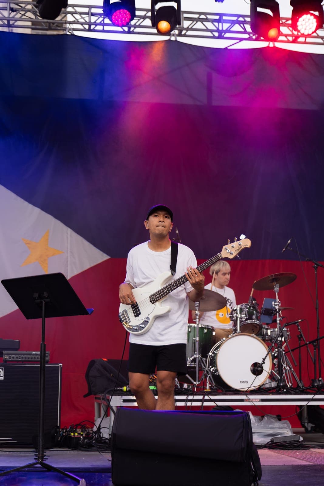 Simplé's bassist stands out front with a white Sterling bass under pink and red wash, the drummer working behind him against the Philippine flag