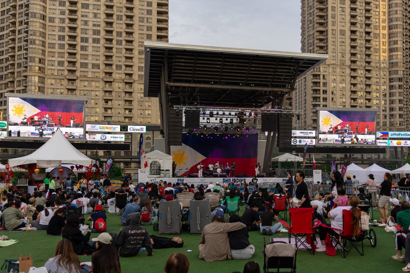 Simplé play the main stage at Mississauga Celebration Square as the crowd watches from lawn chairs and picnic blankets, the band mirrored on the two big screens flanking the stage