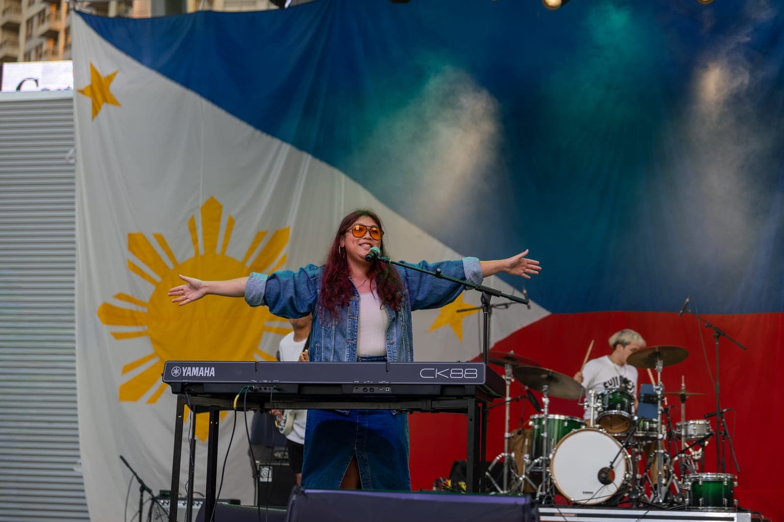 Simplé's vocalist throws both arms wide at her keyboard mid-song, the Philippine flag's golden sunburst filling the frame behind her