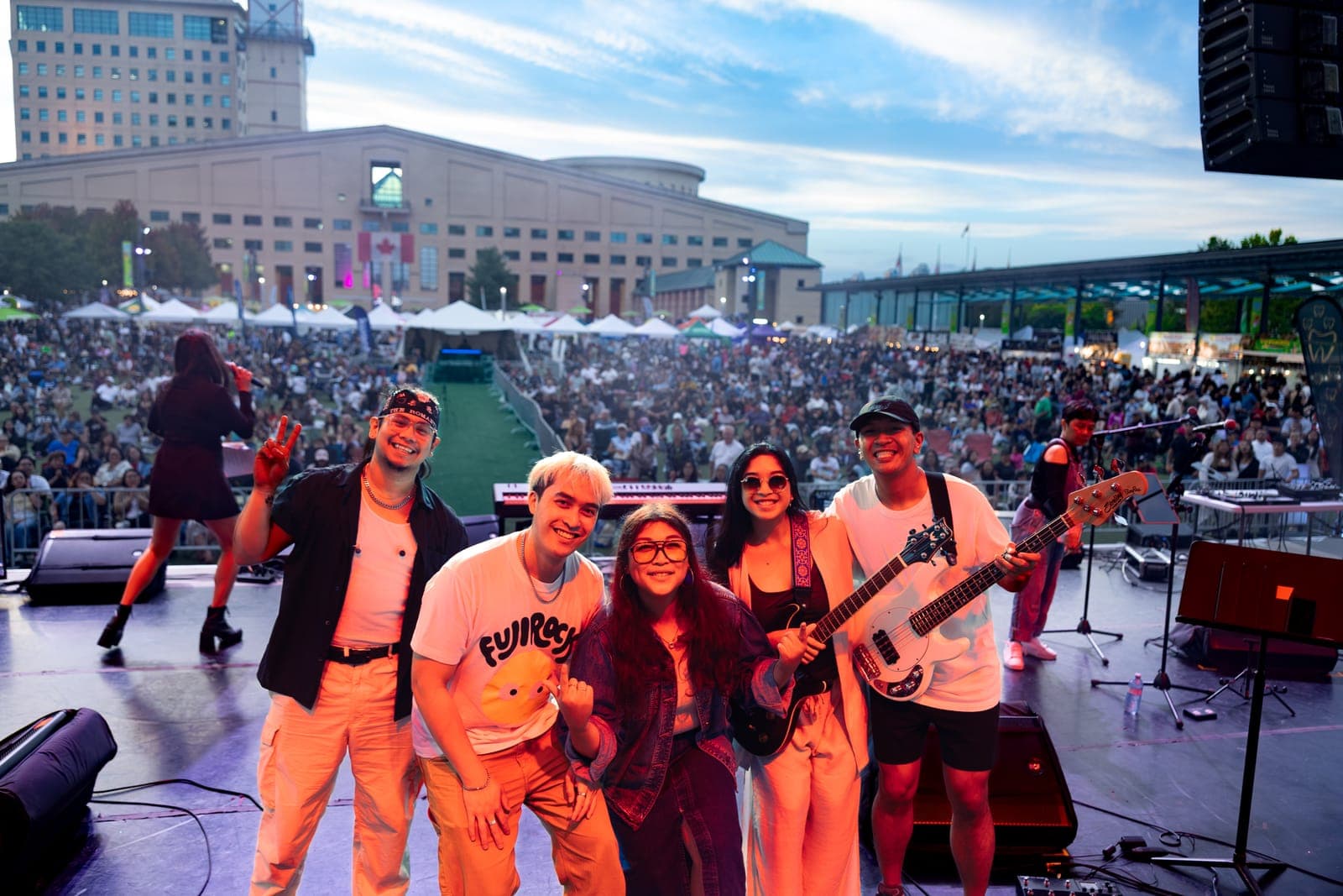 Simplé crowd together for a photo at the edge of the stage after their set, the Mississauga Civic Centre and a lawn full of festival-goers spread out behind them
