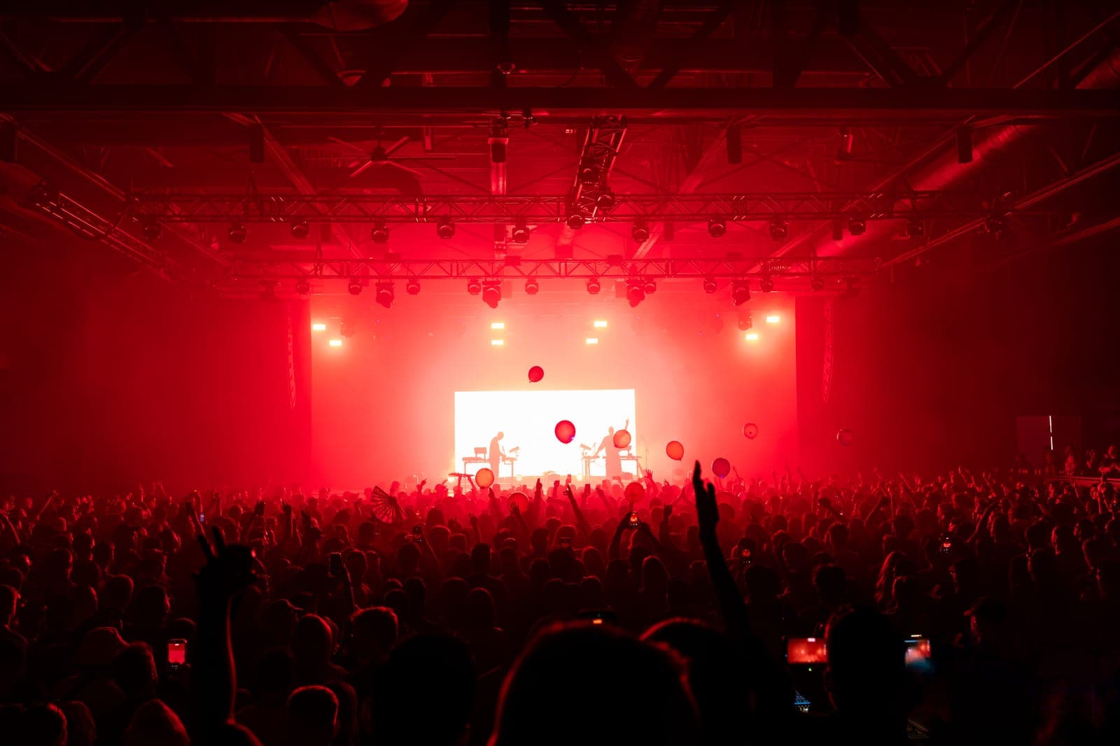 Red balloons drift above the crowd at HISTORY while Tinlicker play in silhouette against a wall of white light