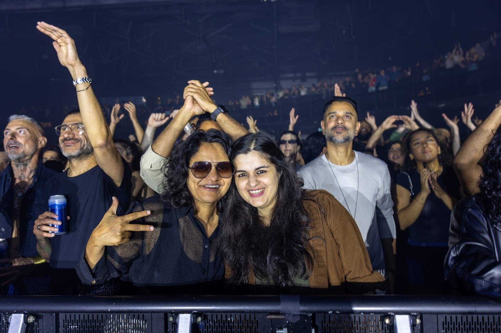 Two fans lean in together at the HISTORY barricade, arms raised across the crowd behind them during Tinlicker's set