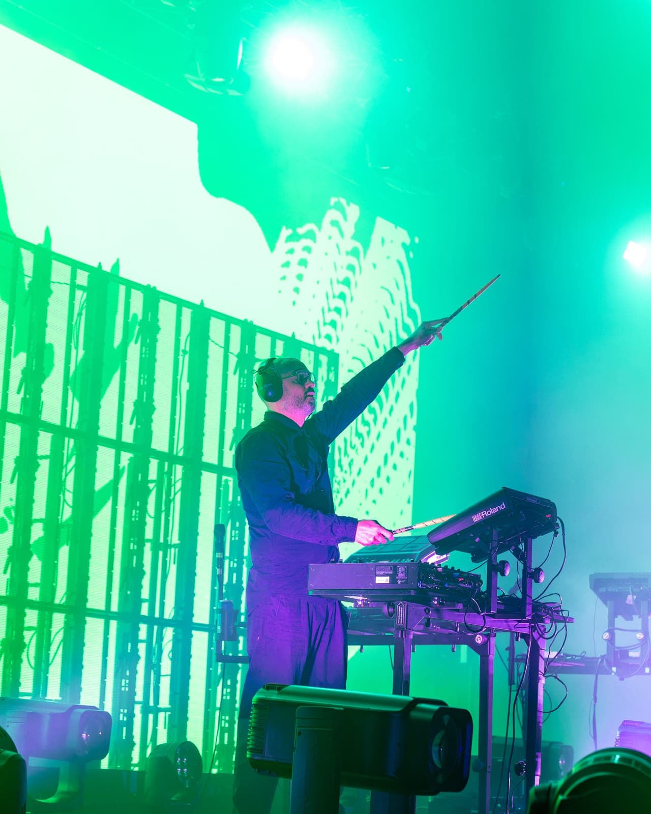 Tinlicker's Micha Heyboer points a stick skyward over his Roland rig, green LED visuals filling the screen behind him