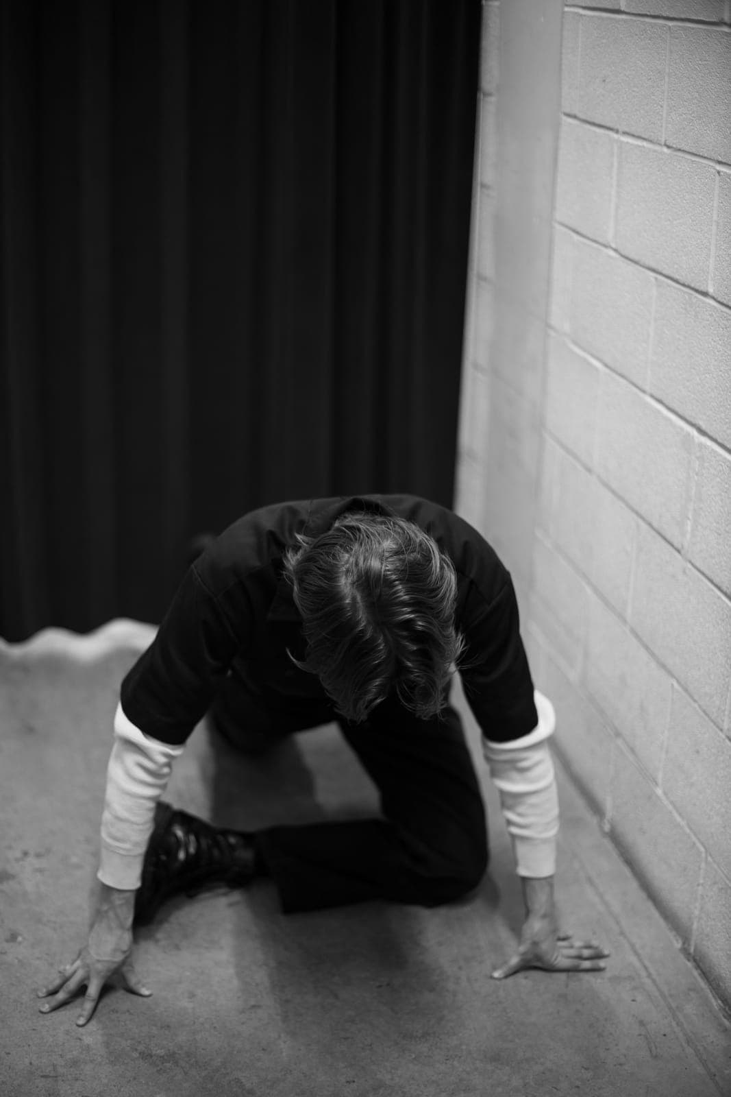 Black-and-white shot of a Black Pontiac member crouched on the floor against a brick wall at The Drake Underground