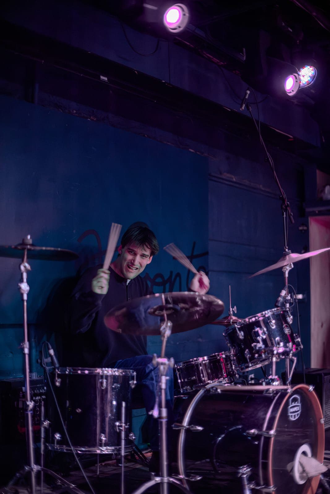 Black Pontiac's drummer mid-strike with sticks raised under purple light at The Drake Underground