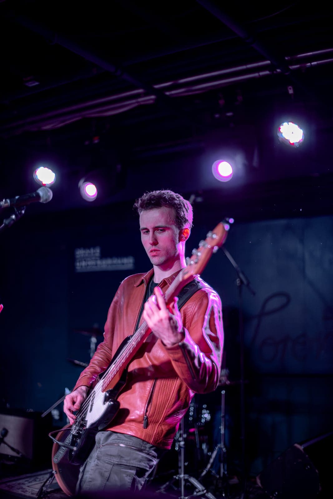 Black Pontiac guitarist in a brown leather jacket playing under pink stage light at The Drake Underground, Toronto