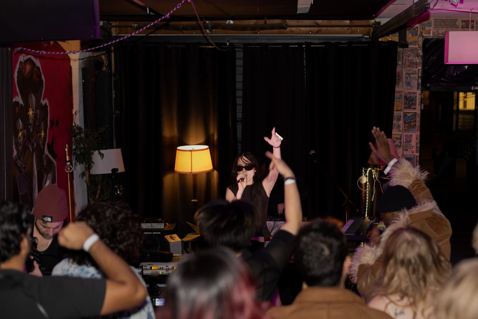 City Builders' vocalist performs under a warm lamp as the crowd's hands rise in the foreground at Division 88 in Toronto