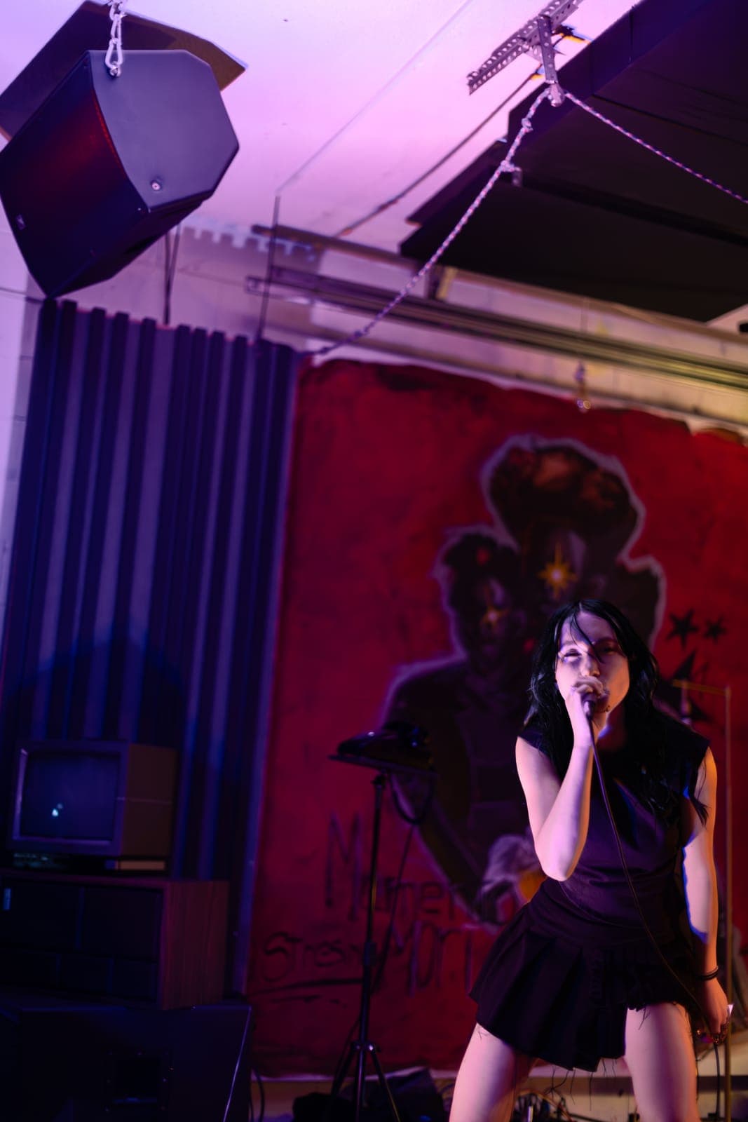 City Builders' vocalist sings beneath a hanging speaker in front of a red painted figure at Division 88, Toronto