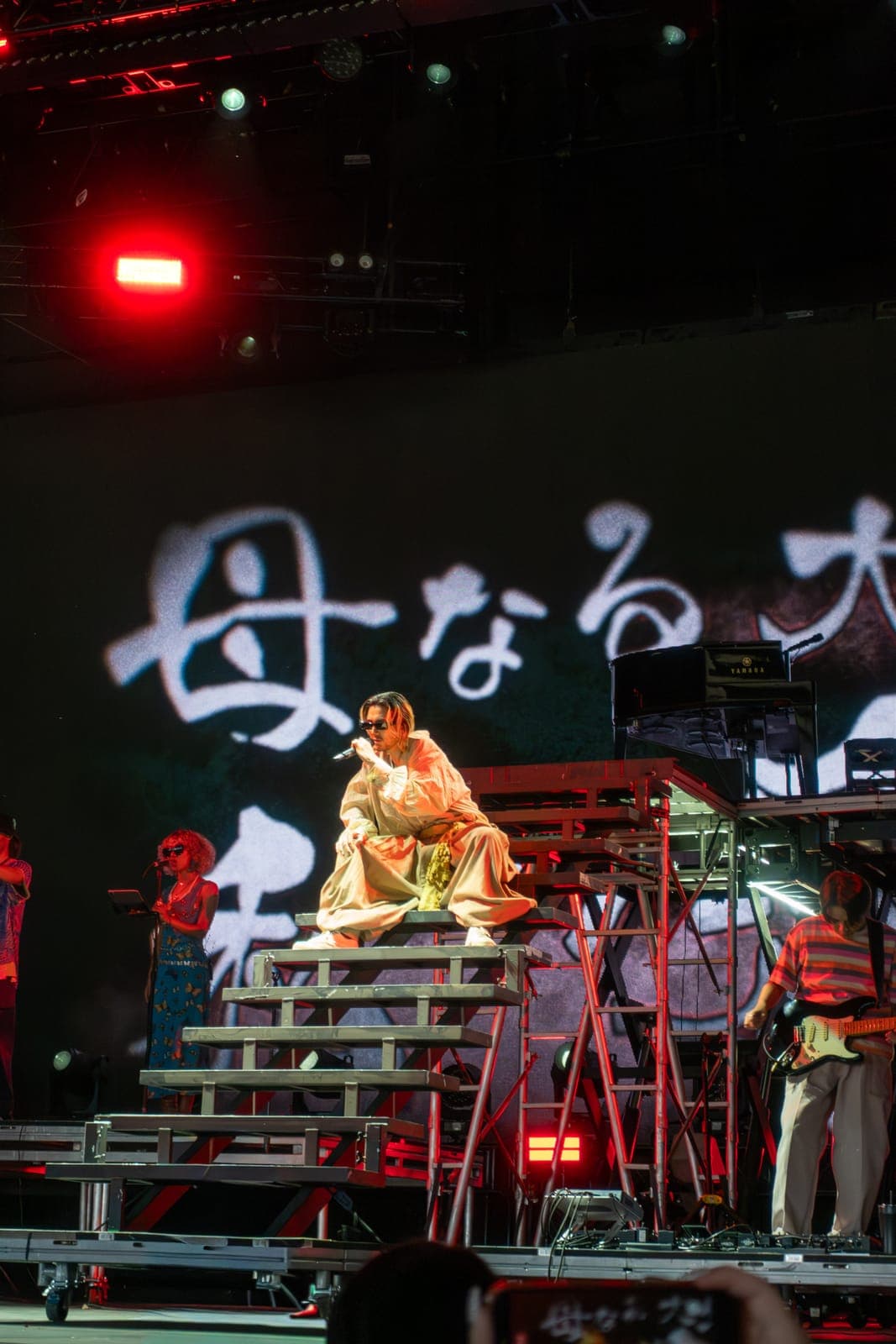 Fujii Kaze sits atop a platform in flowing robes with Japanese lyrics projected behind him at Coachella, Indio