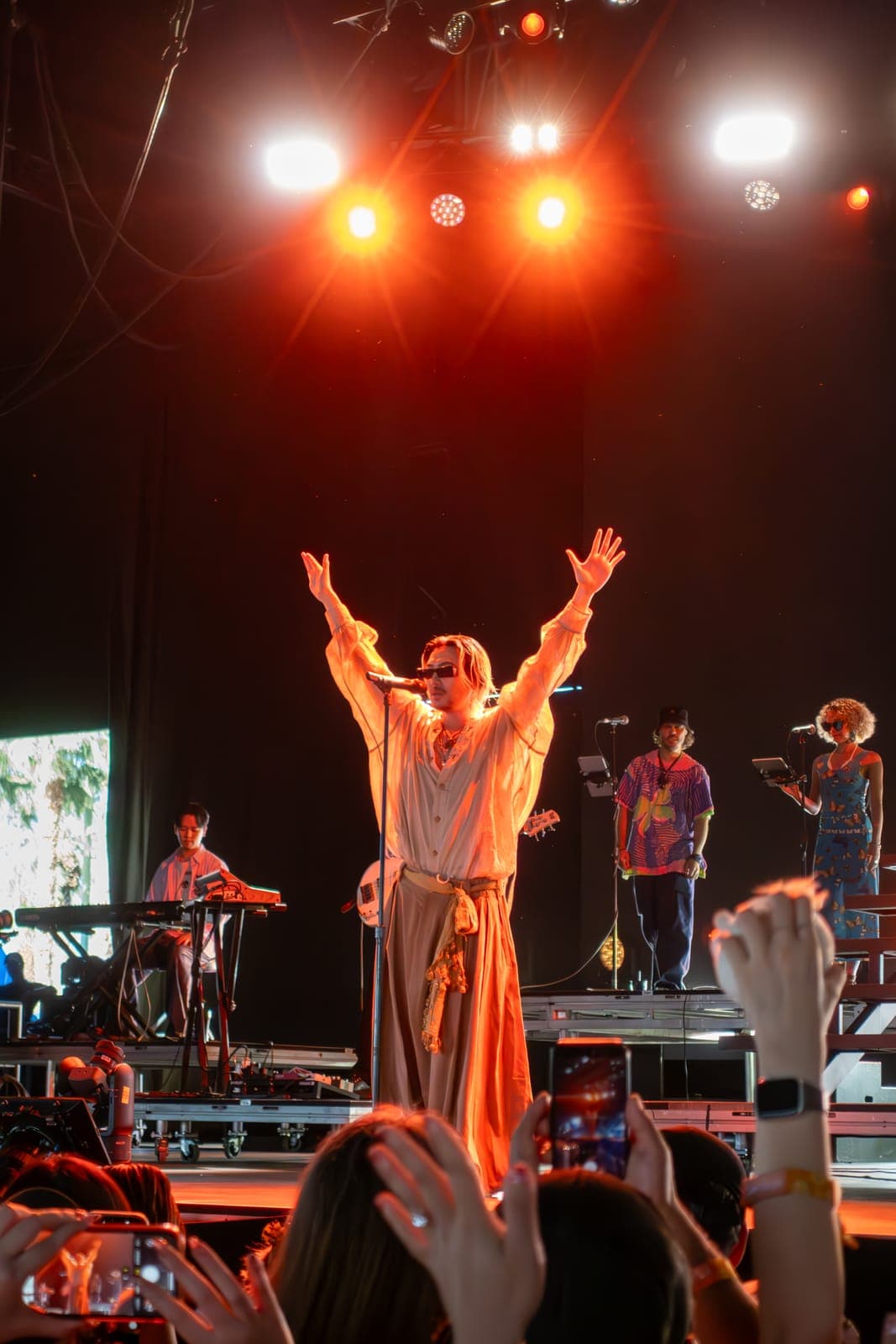 Fujii Kaze throws his arms wide under warm light as the Coachella crowd films from below at Empire Polo Club in Indio