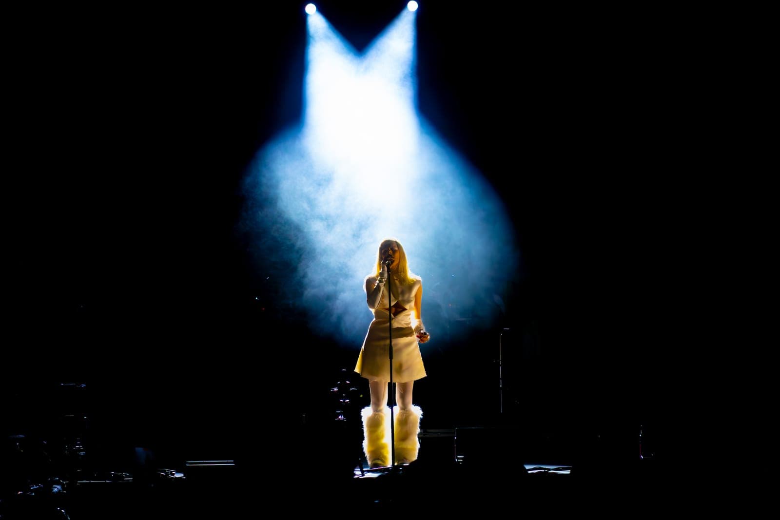 Tomora stands alone in a spotlight and haze, a dramatic silhouette in white at Coachella, Empire Polo Club in Indio