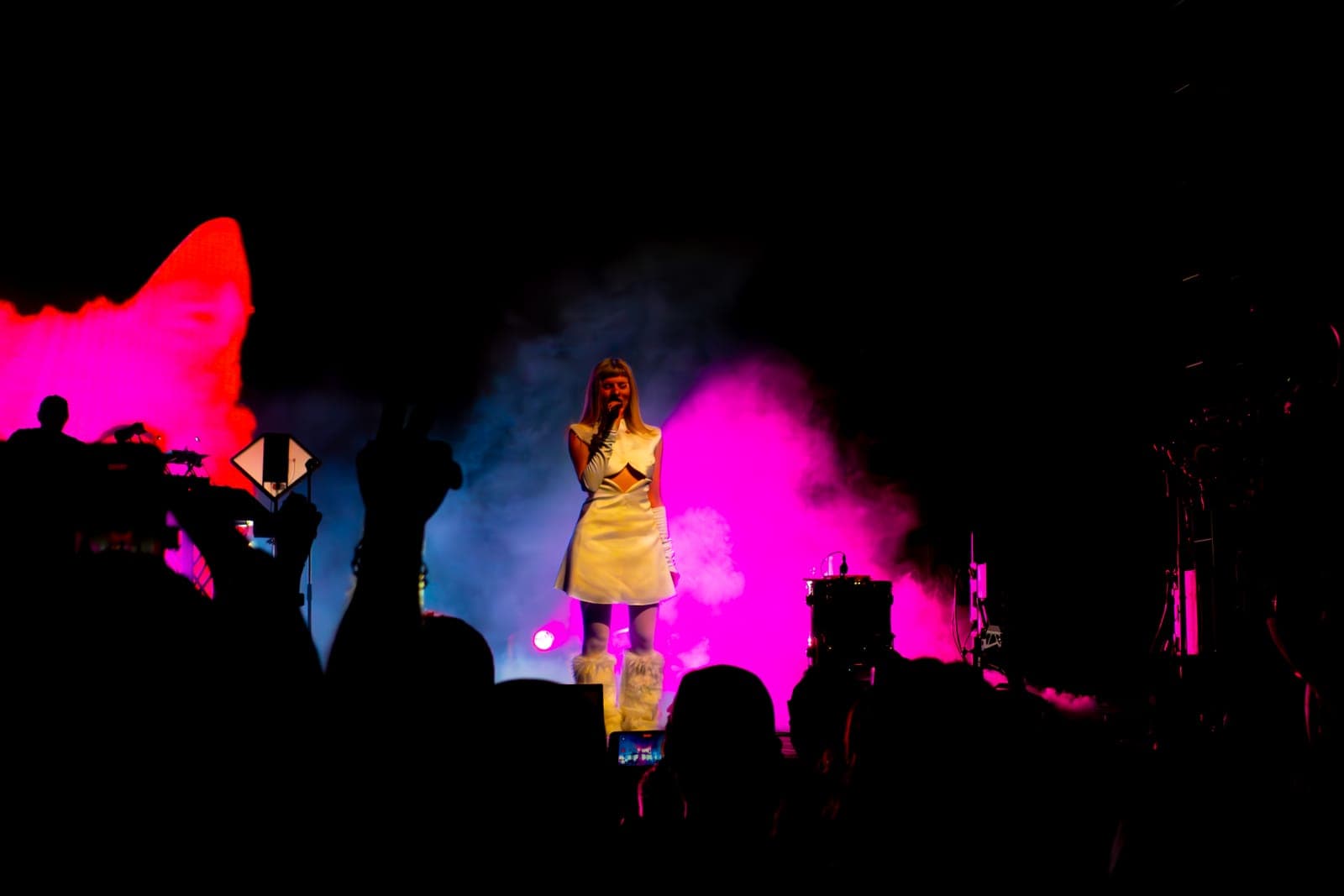 Tomora in a white cut-out dress sings amid pink haze as the crowd reaches up at Coachella, Indio