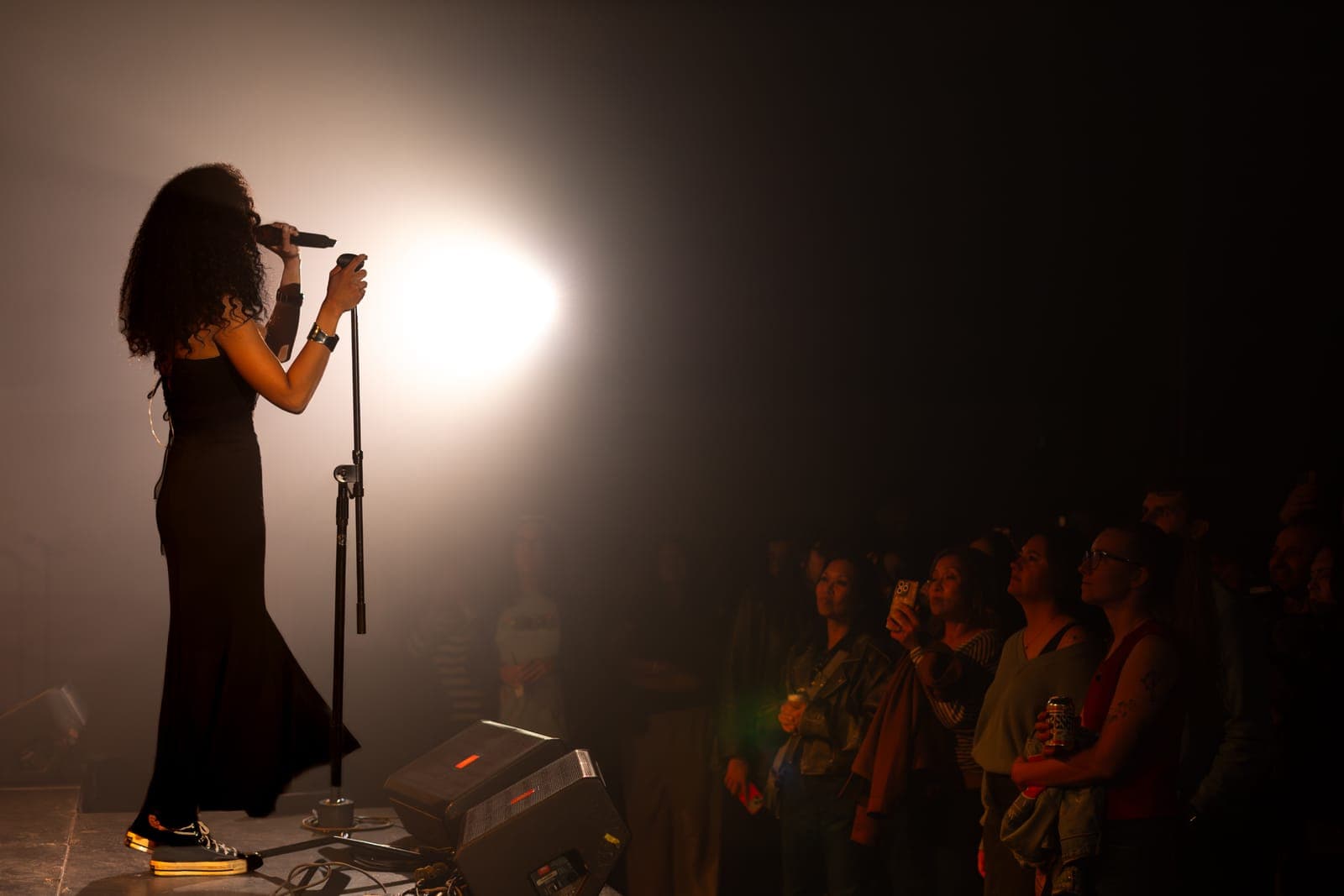 Nia Nadurata silhouetted at the mic against a bright spotlight as the crowd watches at Longboat Hall, Toronto