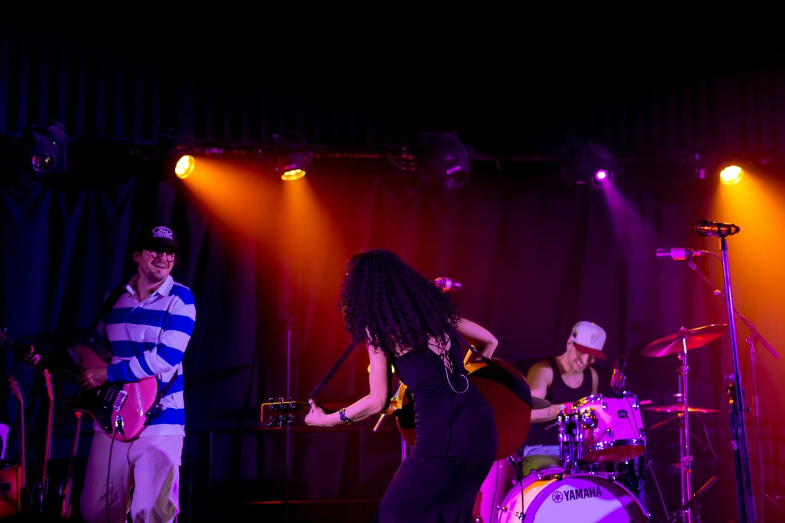 Nia Nadurata dances with her back to the crowd between her guitarist and drummer at Longboat Hall in Toronto