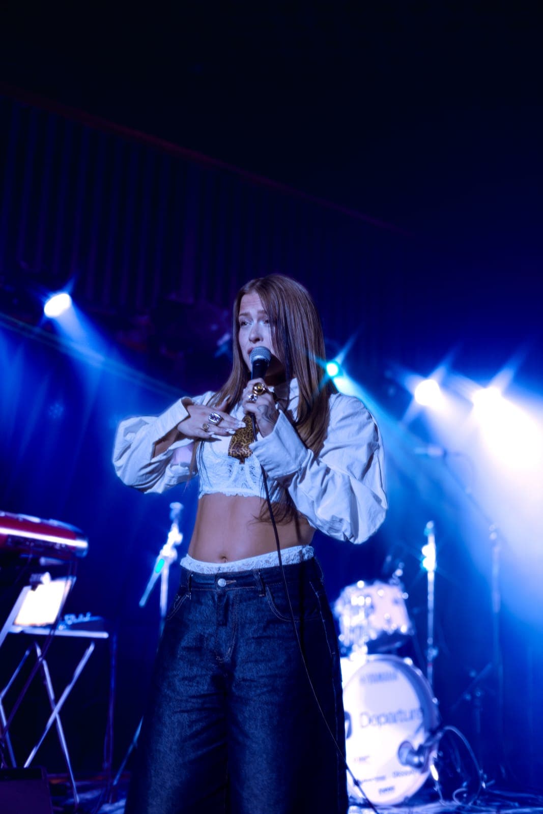 Puma June sings into the mic with both hands in a white cropped jacket under blue side-light at Longboat Hall, Toronto