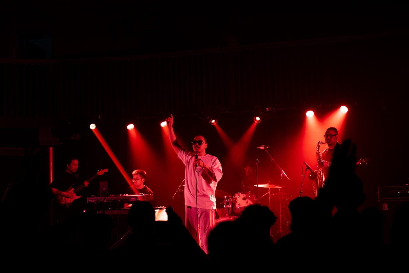Cherry Kim points skyward fronting his full band, saxophone and all, under red light at Longboat Hall in Toronto