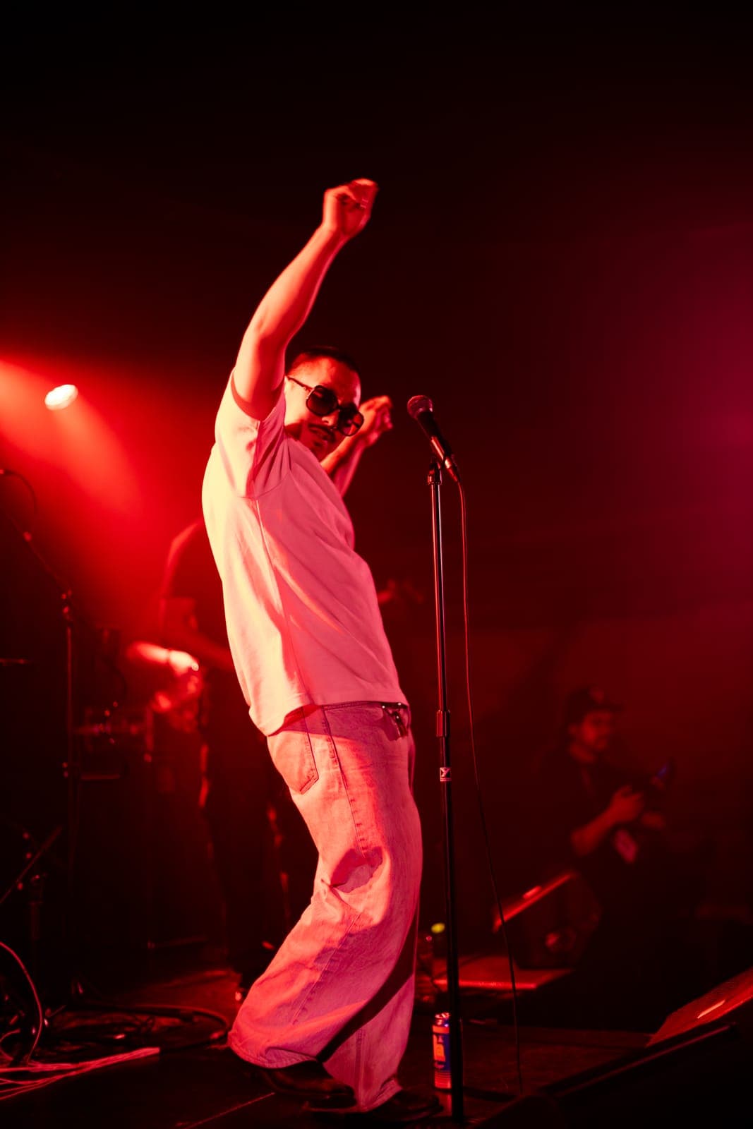 Cherry Kim throws a fist up at the mic, bathed in red light, at Longboat Hall in Toronto