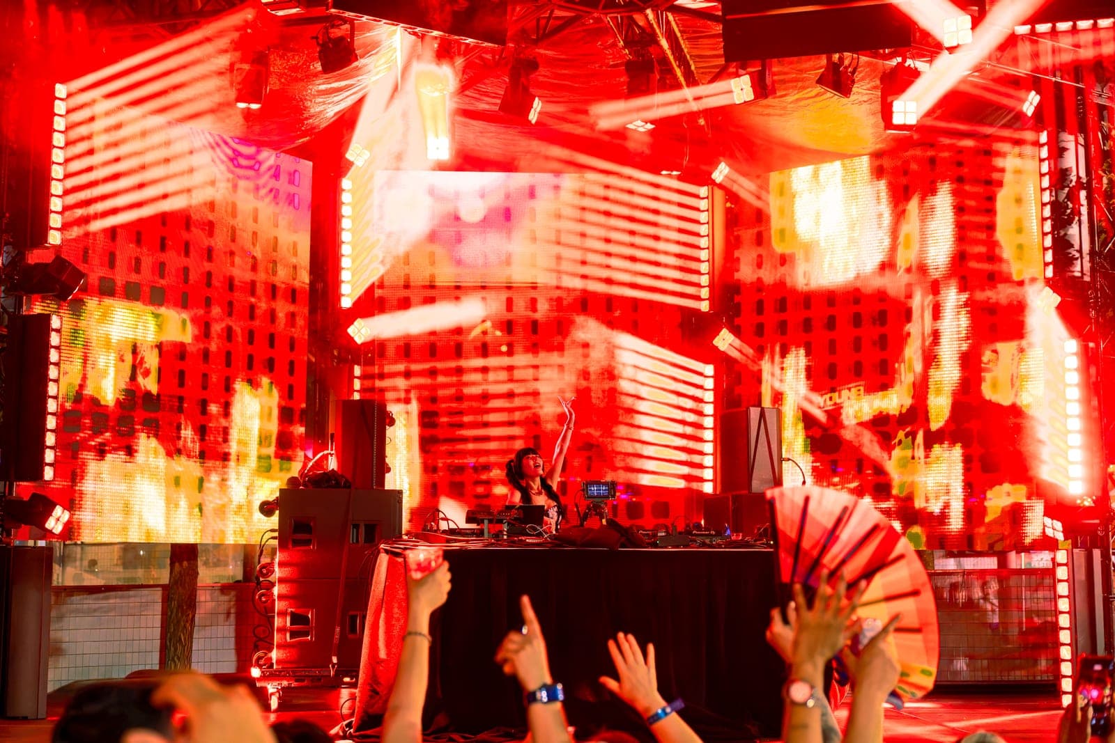 Youna lifts an arm and looks up as red and gold visuals blaze across the stage.