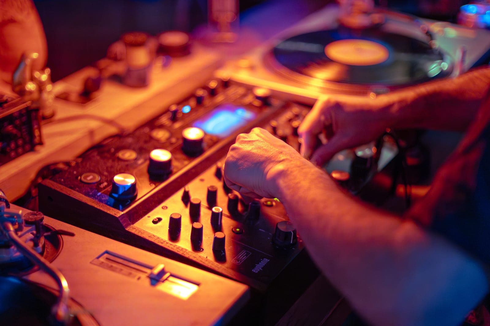 Close-up of hands working a vintage mixer and turntable, vinyl spinning, under warm light at 915 Dupont, Toronto