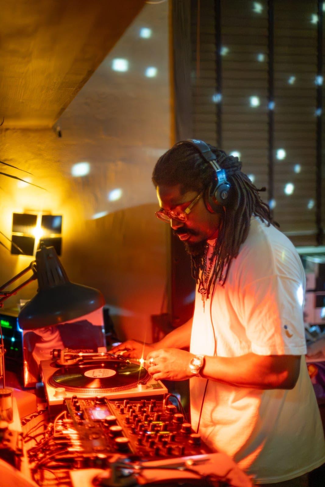 Kiinjo cues a record in headphones at the turntables under warm light at 915 Dupont in Toronto
