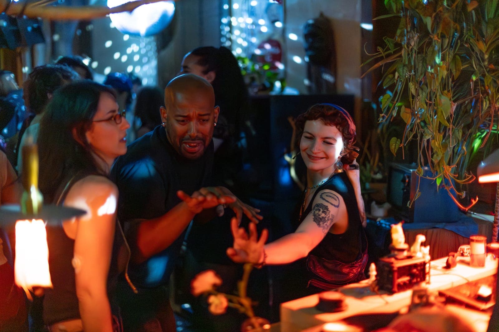 Friends laugh and dance beside the DJ booth amid plants and warm light at 915 Dupont, Toronto
