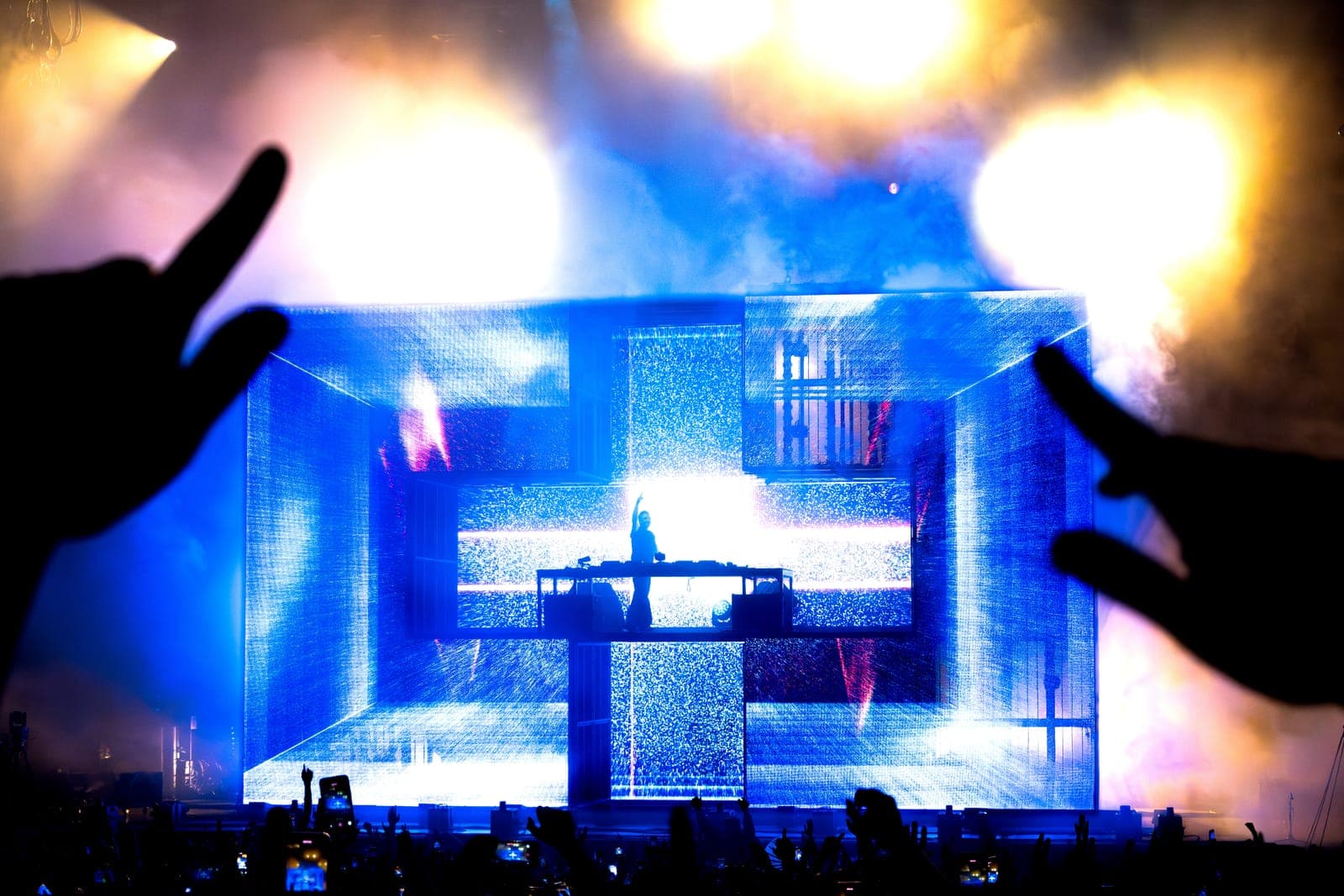 Martin Garrix DJs inside the glowing blue cube stage, framed by a fan's hands, at RBC Amphitheatre in Toronto