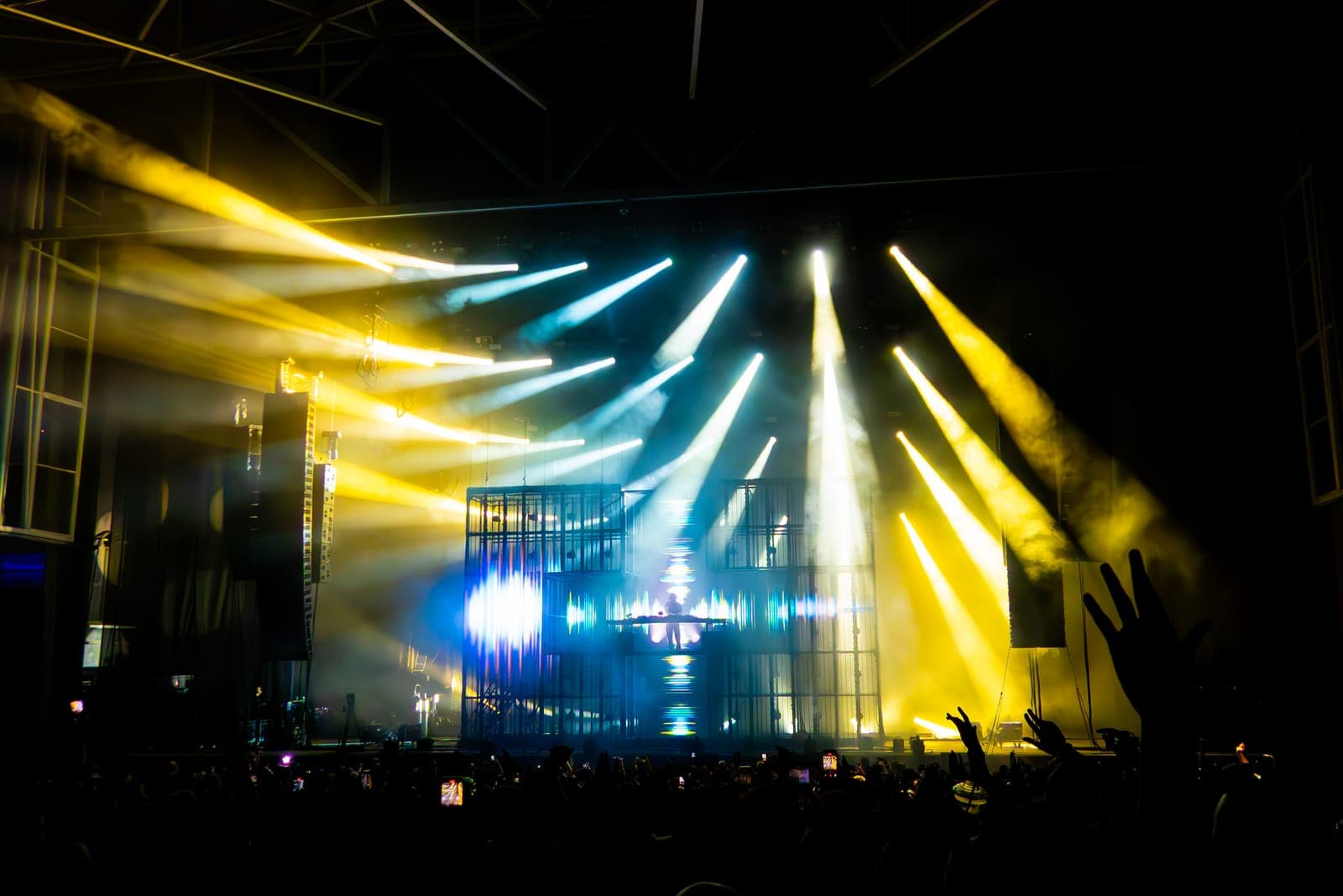 Martin Garrix DJs within a glowing blue cross-shaped screen, framed by a fan's hands, at RBC Amphitheatre in Toronto