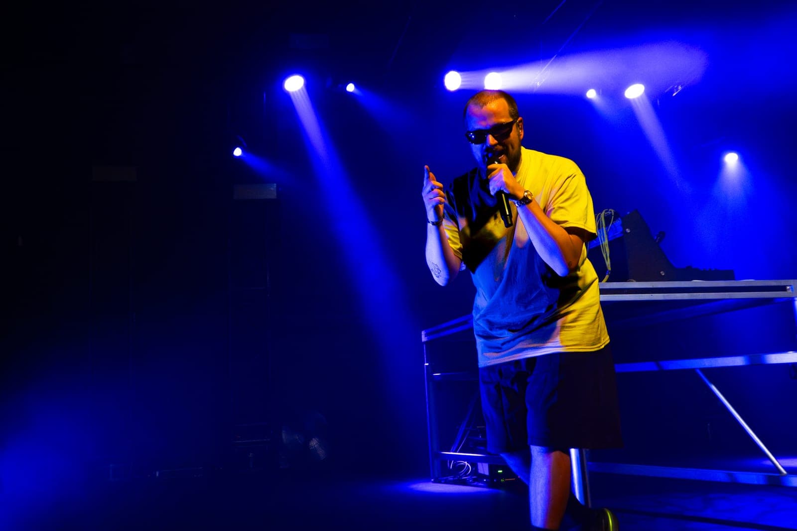 Myd sings into the mic in a yellow tee and sunglasses under blue light at The Mod Club in Toronto
