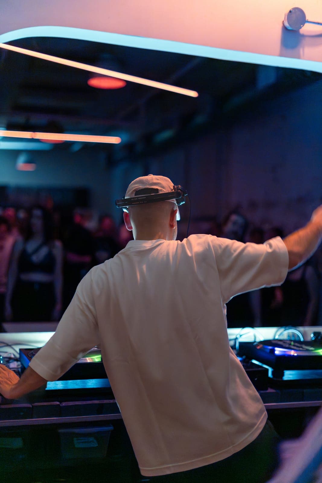 Kiinjo reaches out to the crowd from behind the decks in a white cap and headphones at Standard Time in Toronto
