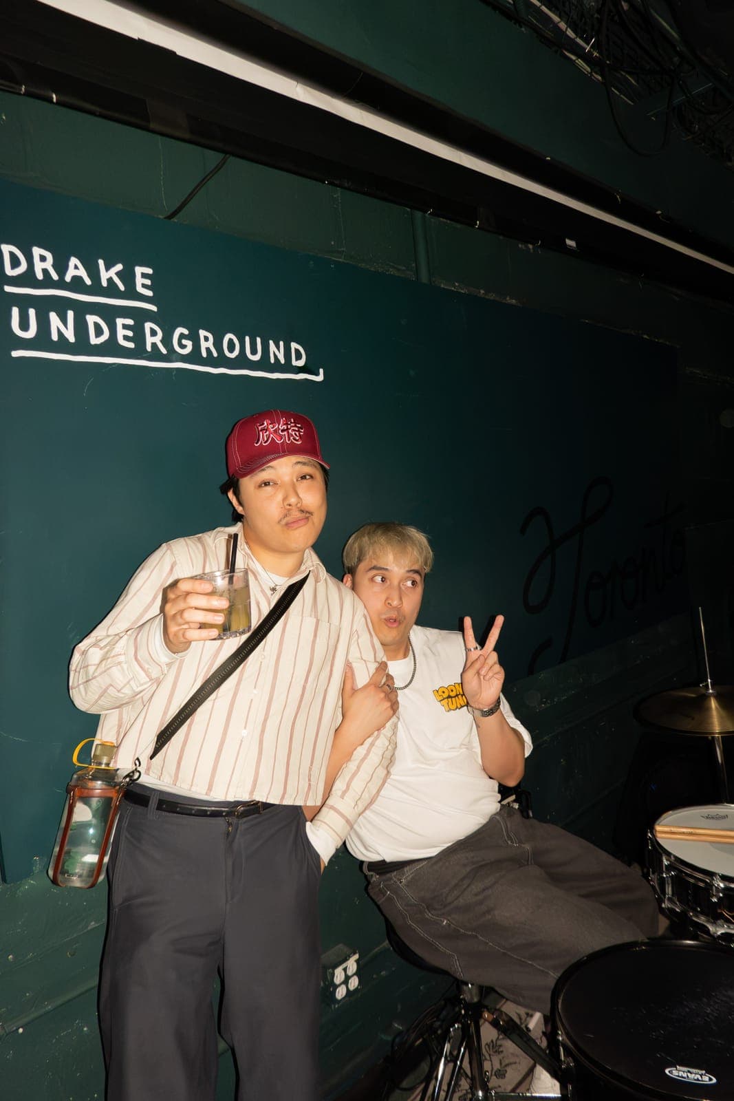Two Takes a Village members pose against the green backstage wall at The Drake Underground in Toronto