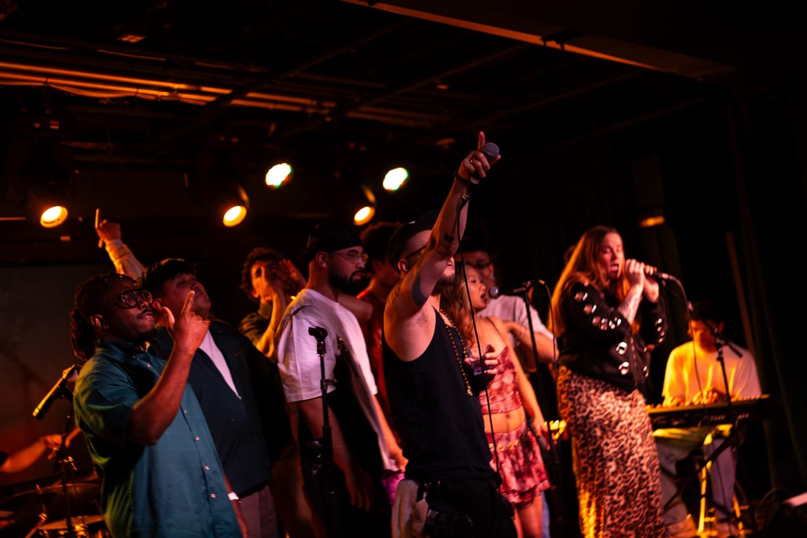 The Takes a Village singers crowd the front of the stage, one pointing skyward, at The Drake Underground in Toronto
