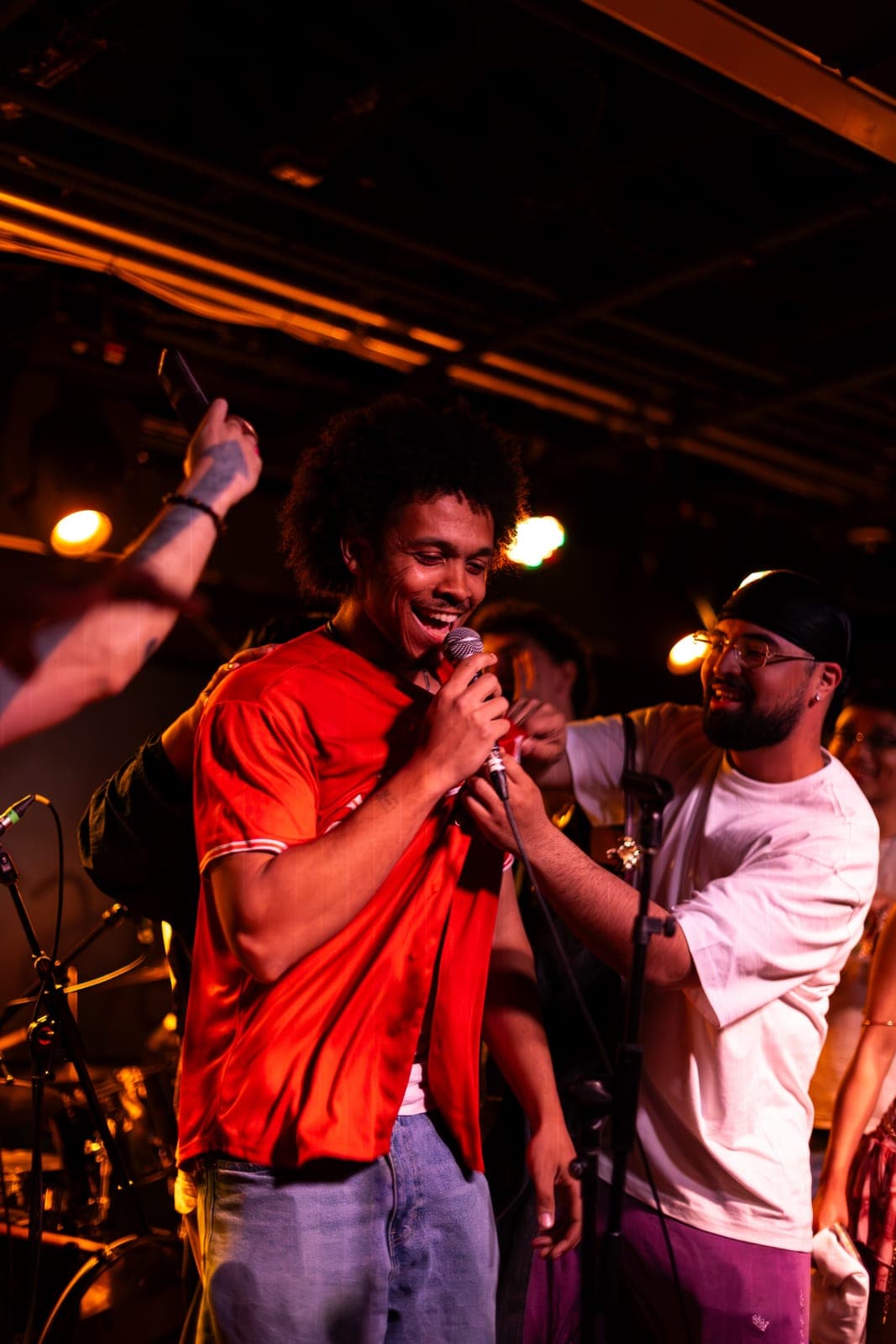 A Takes a Village vocalist with an afro sings into the mic in a red tee at The Drake Underground in Toronto