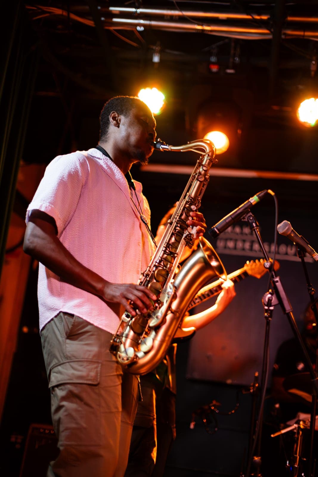 A Takes a Village saxophonist plays in profile under warm stage lights at The Drake Underground in Toronto